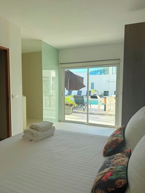 A hotel room with a bed, a large window, and a view of a pool and outdoor seating.