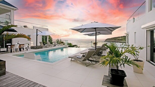 Ein moderner Poolbereich im Freien mit Liegestühlen und Sonnenschirmen, mit Blick auf das Meer.