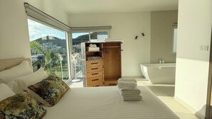 Ein Schlafzimmer mit einem großen Bett, einem Holzschrank, einem Badezimmer mit einer Badewanne und Blick auf die Stadt.