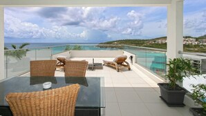 A balcony with wicker furniture, a glass table, and a potted plant.