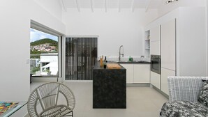 A modern kitchen with a central island, a dining area with a wicker chair, and a sofa.