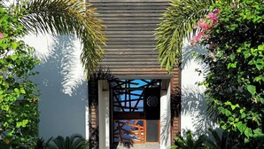 A modern entrance with a wooden slatted door, potted plants, and a paved pathway leading to a building.
