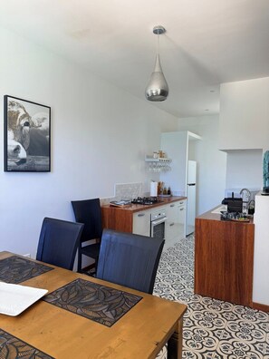 A modern kitchen with a central island, a dining area with a wooden table and chairs, and a hanging pendant light.