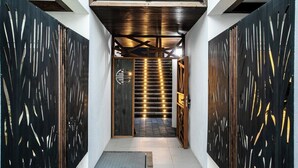 Ein schmaler Korridor mit Holzbalkendecke, einer Treppe mit beleuchteten Stufen und einem dekorativen Metallgeländer auf beiden Seiten.