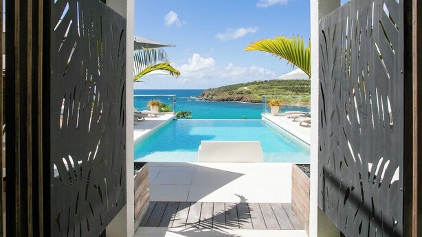 Ein Pool ohne Ende mit Blick auf den Ozean, umgeben von einer Holzterrasse und Palmen.