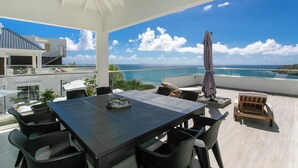 Ein moderner Essbereich im Freien mit Blick auf das Meer, einen Pool und ein Gebäude im Hintergrund.