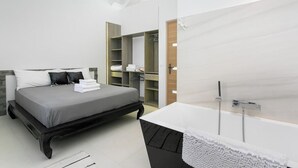 Ein modernes Schlafzimmer mit Bett, begehbarem Kleiderschrank und einem Badezimmer mit großem Spiegel und Badewanne.