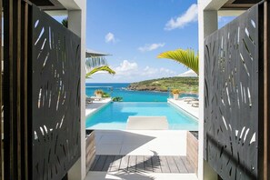 An infinity pool with a view of the ocean, surrounded by a wooden deck and palm trees. - Garden (Apt6) Terrace & Garden, Sea View, Pool View # 2 bedrooms (Sint Maarten)