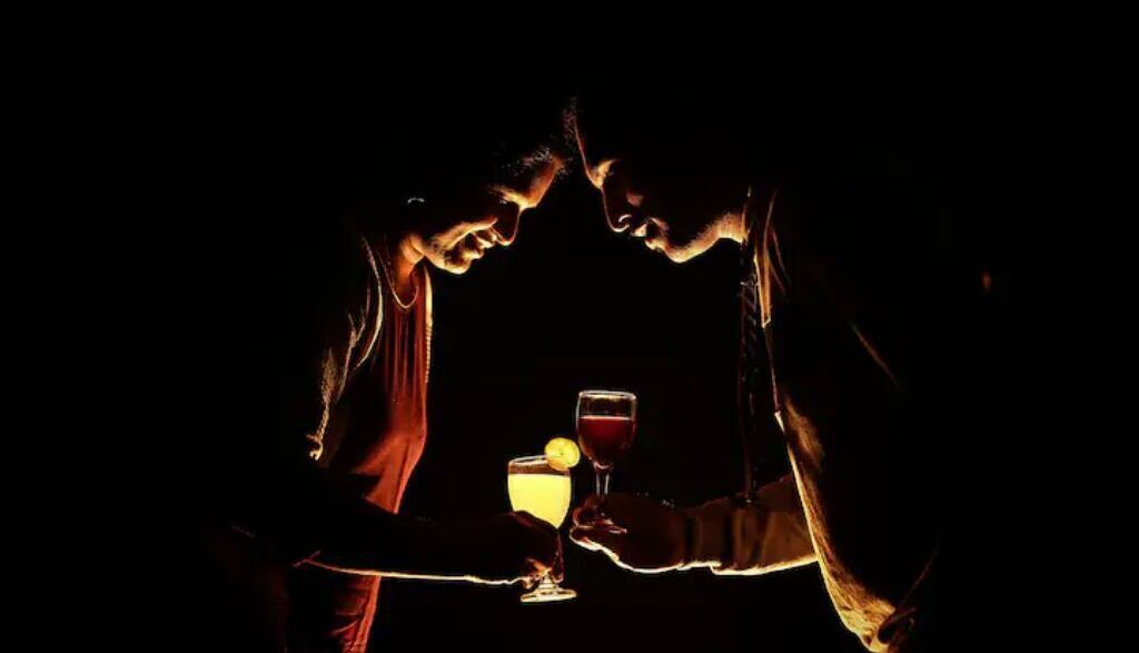 Two people toasting with drinks in a dark setting.