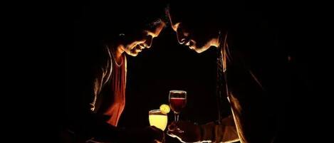 Two people toasting with drinks in a dark setting.