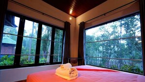 Ein Zimmer mit einem großen Bett, zwei Fenstern und Blick auf einen Wald.