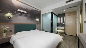A hotel room with a bed, a painting, a bathroom with a sink, and a door.