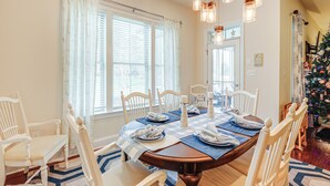 A dining room with a wooden table set for four, white chairs, and a Christmas tree in the background. - Shuttle to Beach: 'Shore Thing' Home in Ocean View (Ocean View)