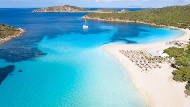 Una zona costera con una playa de arena, un bote y una pequeña isla a lo lejos.