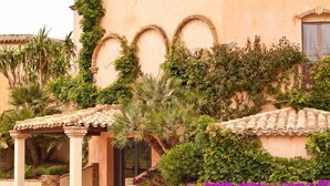 Un edificio con un vestíbulo cubierto, ventanas en arco y abundante vegetación.