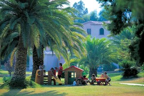 A park with palm trees, a play structure, and a small wooden house. - Shared Pool Apartment in Pula (Pula (CA))
