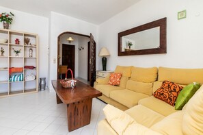 A living room with a sofa, a wooden coffee table, a bookshelf, and a mirror on the wall.