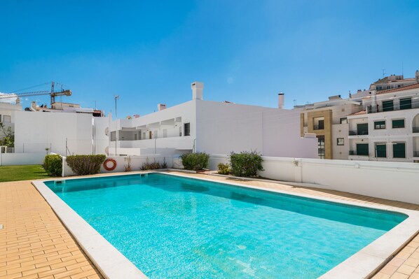 A rectangular swimming pool with a tiled edge, surrounded by a brick patio.