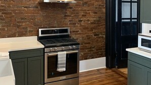 Una cocina con pared de ladrillo, estufa de acero inoxidable y una lámpara colgante moderna.