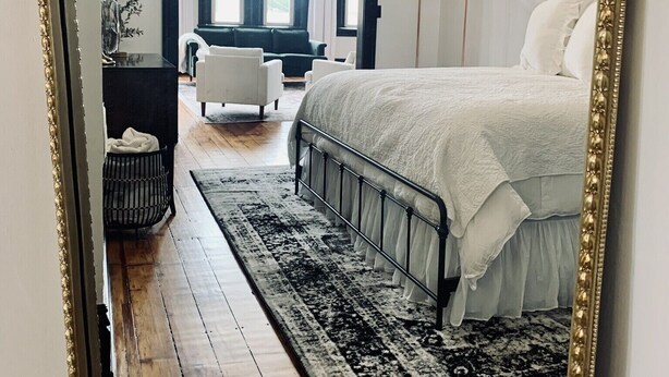 Un dormitorio con una cama grande, una araña, una alfombra blanco y negro y vistas a una ventana con cortinas.