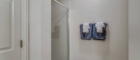 A bathroom with a glass shower door, white walls, and two towels hanging on a towel rack.