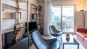 Un soggiorno moderno con una TV a schermo piatto, due poltrone nere, un divano rosso, un tavolino in vetro e una libreria.