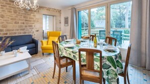 Un coin repas avec une table dressée pour quatre personnes, entourée de chaises, d’un lustre et offrant une vue sur l’extérieur grâce à de grandes fenêtres.