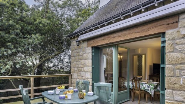 Un bâtiment en pierre doté d’une terrasse en bois et d’une table dressée pour le repas.