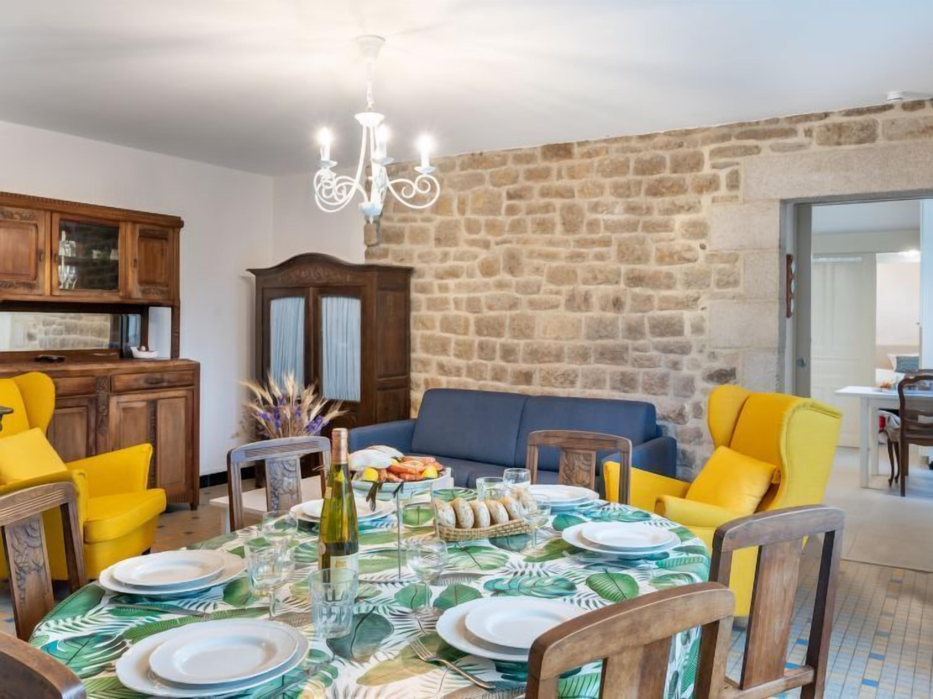 A dining area with a stone wall, wooden furniture, and a chandelier.