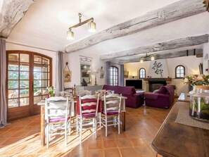 A cozy living room with a dining area, wooden beams, and a fireplace.