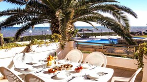 A dining table set outdoors with white chairs, a view of the sea, and a pool in the background. - Laguna Beach Plus by Interhome (Dénia)