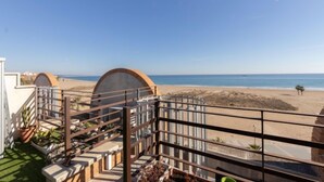 Un balcón con vista a la playa, cielo despejado y un barco a lo lejos.