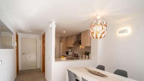 A modern kitchen with white cabinets, a dining area with a white table and grey chairs, and a unique spherical chandelier. - Apartment Sakura by Interhome (Segur de Calafell)