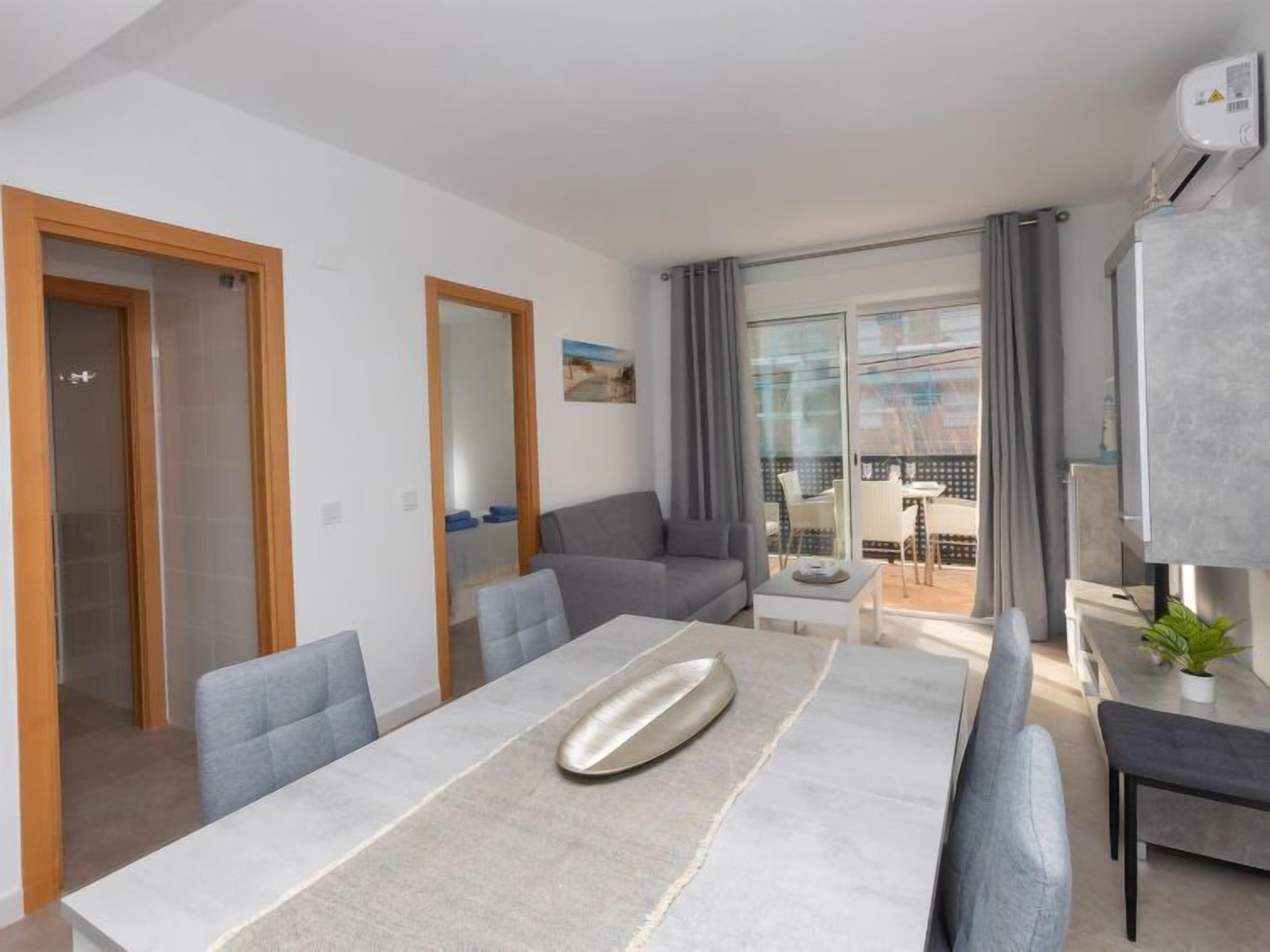 Ein modernes Wohnzimmer mit Esstisch, grauem Sofa und einem Balkon mit Blick.