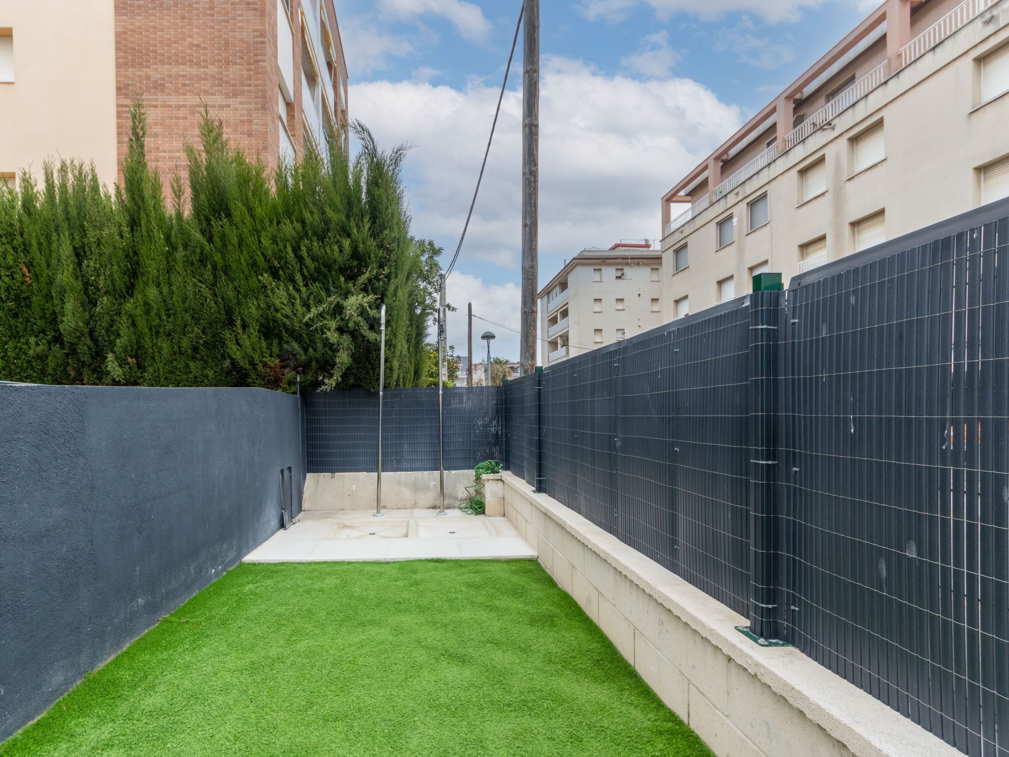A courtyard with artificial green grass, a black metal fence, and a brick building in the background.
