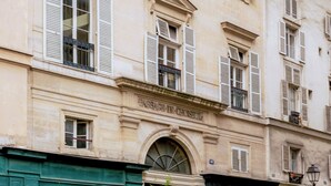 A historic building with classical architecture, featuring multiple windows with shutters, a prominent entrance with a black awning, and a street lamp. - Merveil Luxury Suite - Louvre - Dalayrac (Paris)