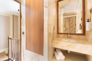 A bathroom with a wooden door, a marble sink, a mirror, and a shower.