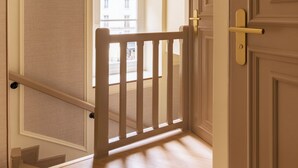 A hallway with a wooden railing, a door with a brass handle, and a view of a building outside. - Merveil Luxury Suite - Louvre - Dalayrac (Paris)