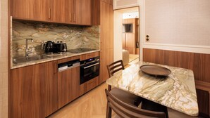 A compact kitchen with wooden cabinets, a marble countertop, a built-in oven, and a dining area with a marble table. - Merveil Luxury Suite - Louvre - Dalayrac (Paris)
