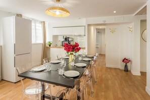 A modern kitchen with white cabinets, a built-in oven, and a dining area with a long table set for six. - Family Suite - Marais - Pelee (Paris)