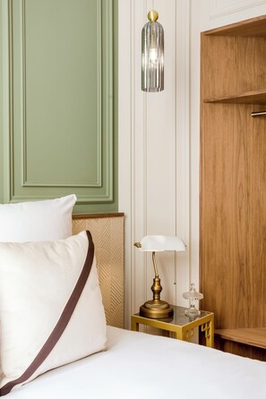 A hotel room with a bed, pillows, a nightstand with a lamp, and a wooden wardrobe.