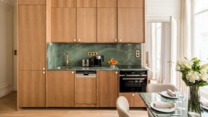 A modern kitchen with wooden cabinets, a green marble countertop, and a dining area with a glass table and chairs. - Merveil - Luxury Suite - Marais - Caire I (Paris)