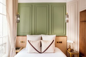 Une chambre d’hôtel avec un lit, une table de chevet, une lampe et une tête de lit verte.