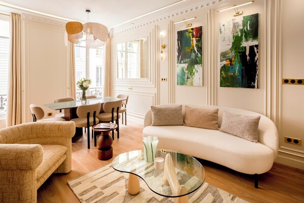 A modern living room with a sofa, chairs, a glass coffee table, and artwork on the walls.