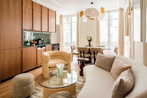 A modern living room with a sofa, armchairs, a glass coffee table, and a dining area with a table and chairs.