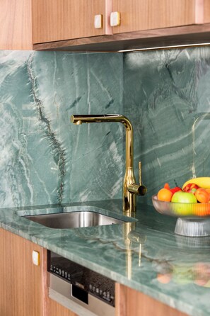 A kitchen with a marble countertop, a gold faucet, and a bowl of fruit.
