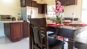 Une cuisine moderne avec des meubles de couleur sombre, un îlot central et un coin repas comprenant une table et des chaises.