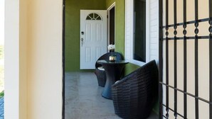 Un espace extérieur abrité, avec une table et des chaises, une porte blanche et un portail en métal.