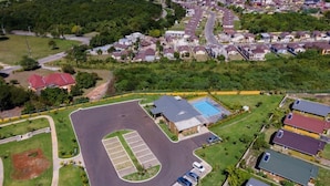 Vue aérienne d’un quartier résidentiel avec un grand parking, une piscine et des maisons aux toits de couleurs variées.