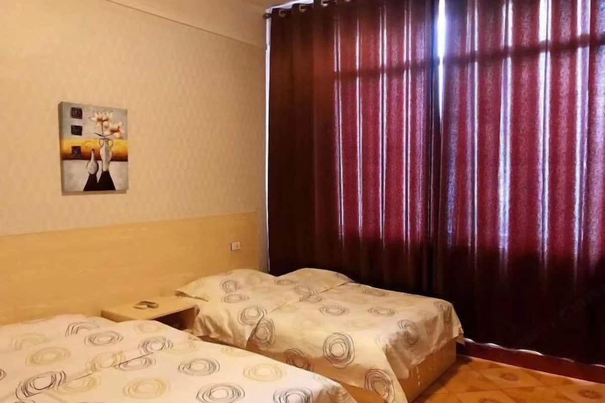 A hotel room with two beds, a painting on the wall, and a window with curtains.